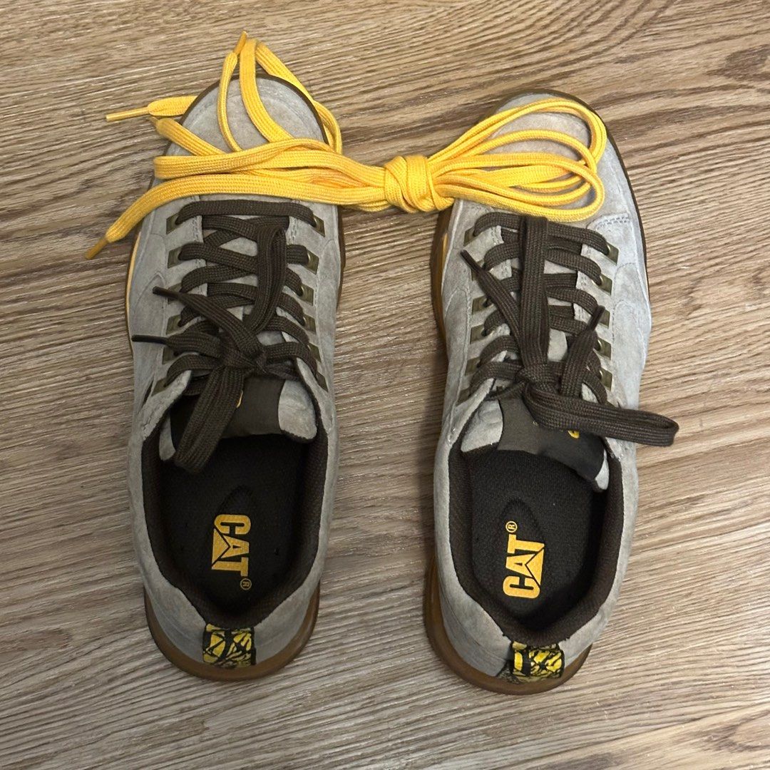 Caterpillar Casual Sneakers Unisex (Category: Sneakers) located in Singapore. Submitted by tequierox (Listing ID 1396379444, Image 2). Description: Lightly used Caterpillar sneakers. Features a grey suede upper with brown laces and a yellow sole. The Caterpillar logo is visible on the insole and side of the shoe. Great for casual wear..