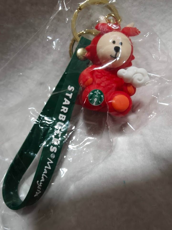 Starbucks Malaysia Year of the Dragon Bearista Keychain (Category: Plushies & Soft Toys) located in Singapore. Submitted by ageless_unicorn (Listing ID 1443870109, Image 4). Description: - Cute Starbucks Malaysia Year of the Dragon keychain - Features the red Dragon Bearista character - Green strap with 'Starbucks Malaysia' text - Comes with a gold keyring - Ideal for attaching to bags or keys - A collectible Starbucks item - 2 for $15.