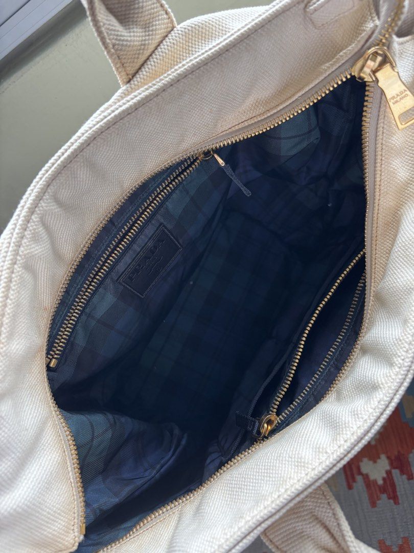 Prada Canvas bucket Tote Bag (Category: Bags & Wallets) located in Singapore. Submitted by forabargain (Listing ID 1444880004, Image 4). Description: - Authentic Prada cream canvas tote bag - Iconic Prada Milano triangle logo - Gold-tone zipper closure - Interior plaid lining with zippered pocket - Sturdy handles - Perfect for everyday use Selling as it is - not for fussy buyers..