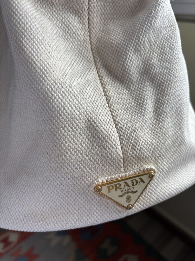 Prada Canvas bucket Tote Bag (Category: Bags & Wallets) located in Singapore. Submitted by forabargain (Listing ID 1444880004, Image 2). Description: - Authentic Prada cream canvas tote bag - Iconic Prada Milano triangle logo - Gold-tone zipper closure - Interior plaid lining with zippered pocket - Sturdy handles - Perfect for everyday use Selling as it is - not for fussy buyers..