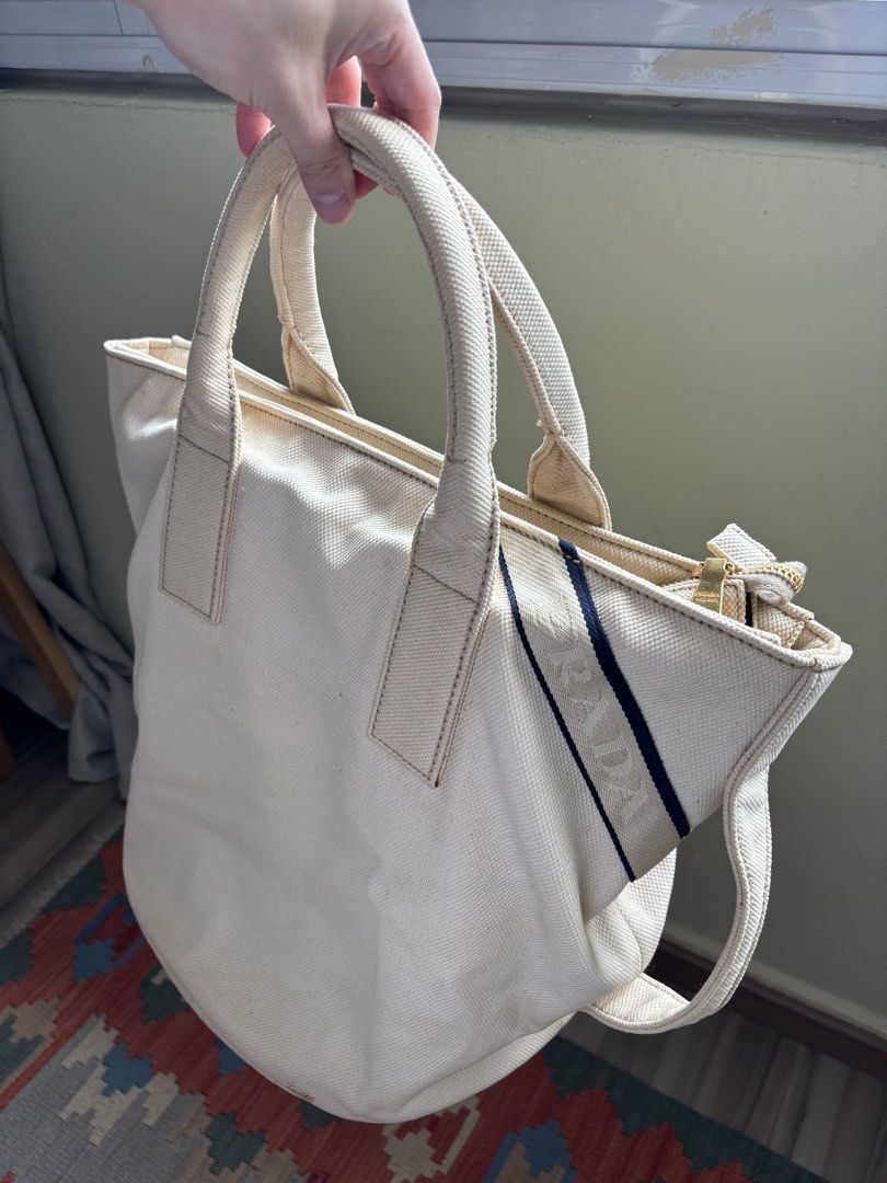 Prada Canvas bucket Tote Bag (Category: Bags & Wallets) located in Singapore. Submitted by forabargain (Listing ID 1444880004, Image 1). Description: - Authentic Prada cream canvas tote bag - Iconic Prada Milano triangle logo - Gold-tone zipper closure - Interior plaid lining with zippered pocket - Sturdy handles - Perfect for everyday use Selling as it is - not for fussy buyers..