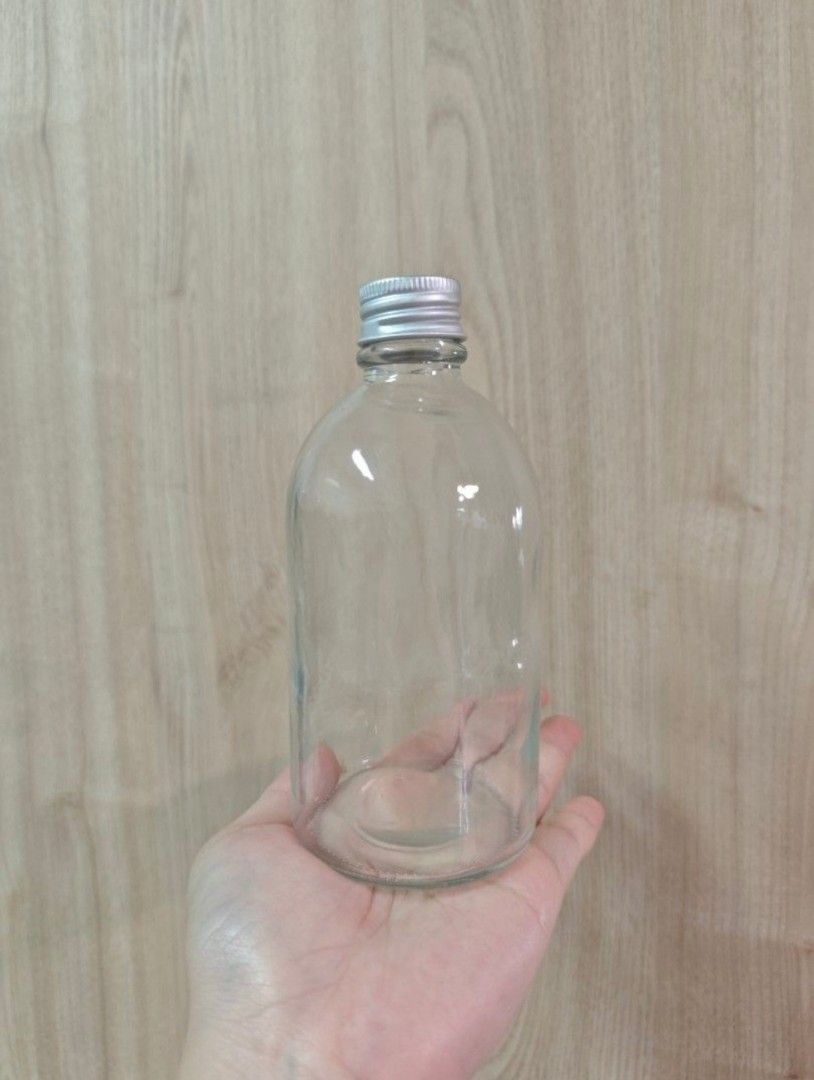 Clear Glass Bottles (280ml) with Silver Caps (Category: Water Bottles & Tumblers) located in Singapore. Submitted by sjliebtcraft (Listing ID 1447888364, Image 5). Description: - Clearing brand new 280ml glass bottles from warehouse - Include silver screw-on caps - Versatile for storing liquids, DIY projects, or as small vases - Bottles are empty and clean - Rounded shape with a flat base.