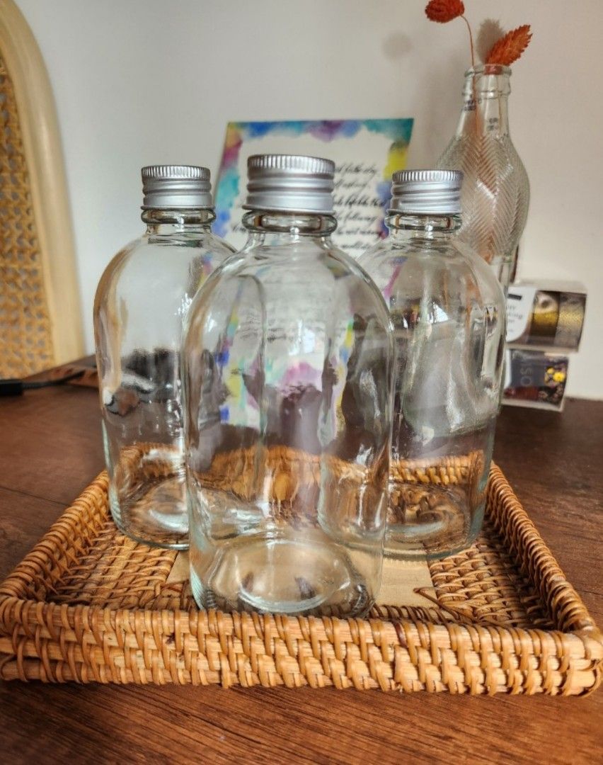 Clear Glass Bottles (280ml) with Silver Caps (Category: Water Bottles & Tumblers) located in Singapore. Submitted by sjliebtcraft (Listing ID 1447888364, Image 1). Description: - Clearing brand new 280ml glass bottles from warehouse - Include silver screw-on caps - Versatile for storing liquids, DIY projects, or as small vases - Bottles are empty and clean - Rounded shape with a flat base.