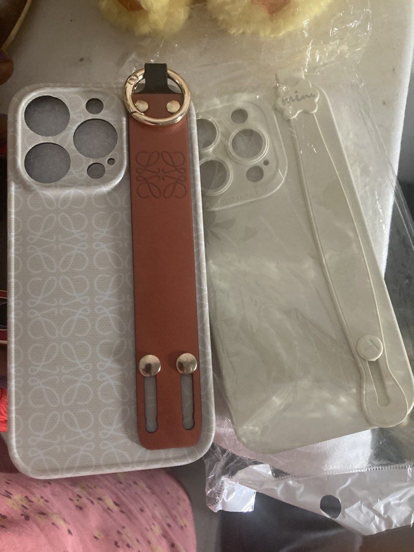 Loewe iPhone Case with Brown Leather Strap (Category: Cases & Sleeves) located in Singapore. Submitted by happysoul9 (Listing ID 1458769694, Image 1). Description: - Loewe phone case set - Suitable for iPhone - Features brown leather strap with gold hardware - Case has a subtle all-over pattern - Includes a clear phone case with a strap - Offers stylish phone protection.